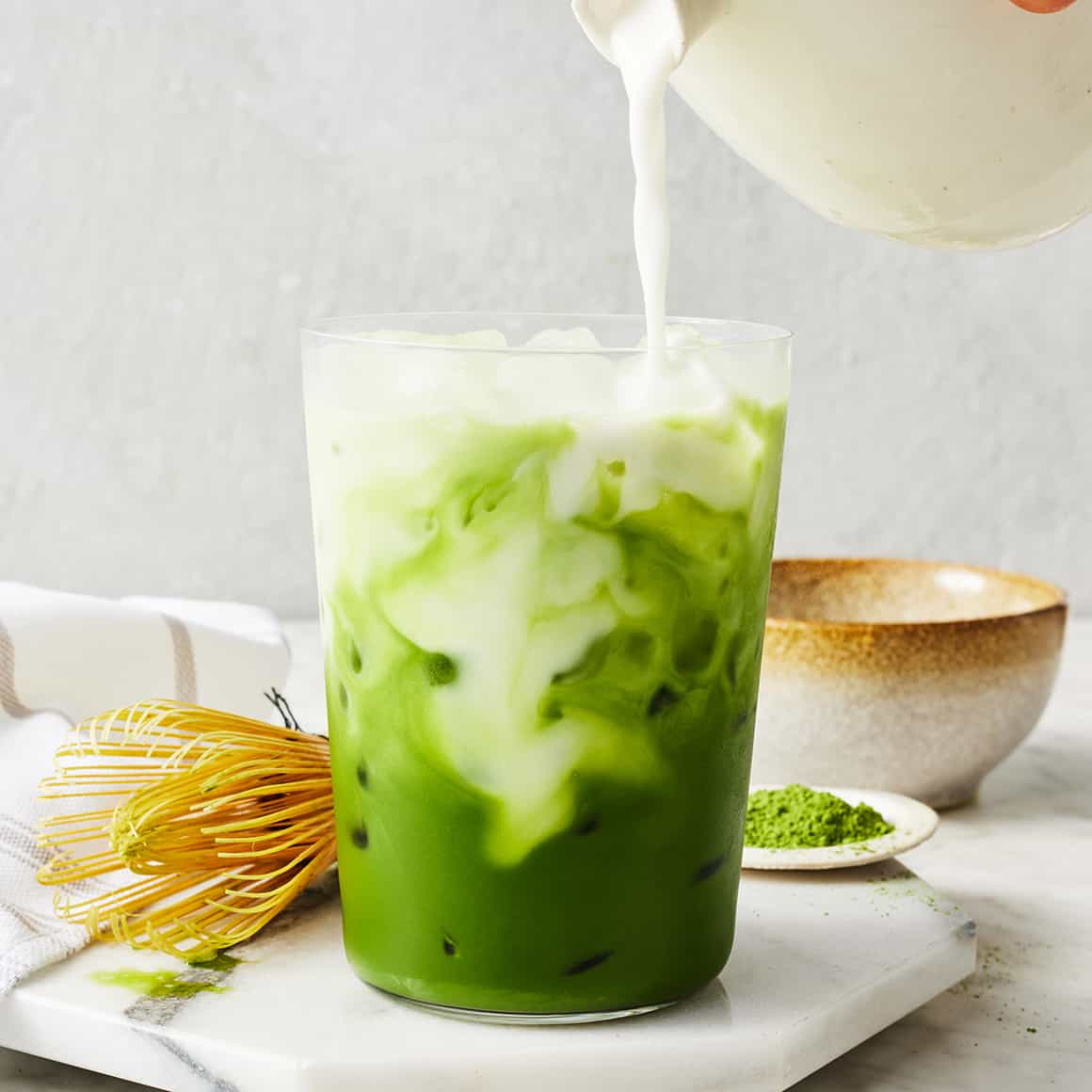 a yummy-looking matcha latte with green matcha at the bottom and swirls of milk being poured in.