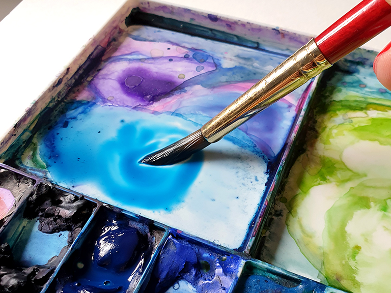 a mix of colorful blue and purple watercolor paints on a palette.