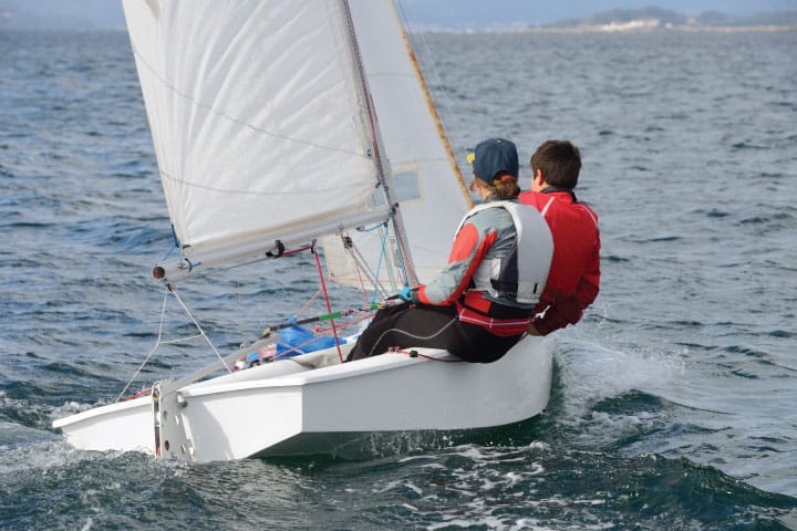 a beginner sailboat on the water, with two people in it maneuvering the sailboat.